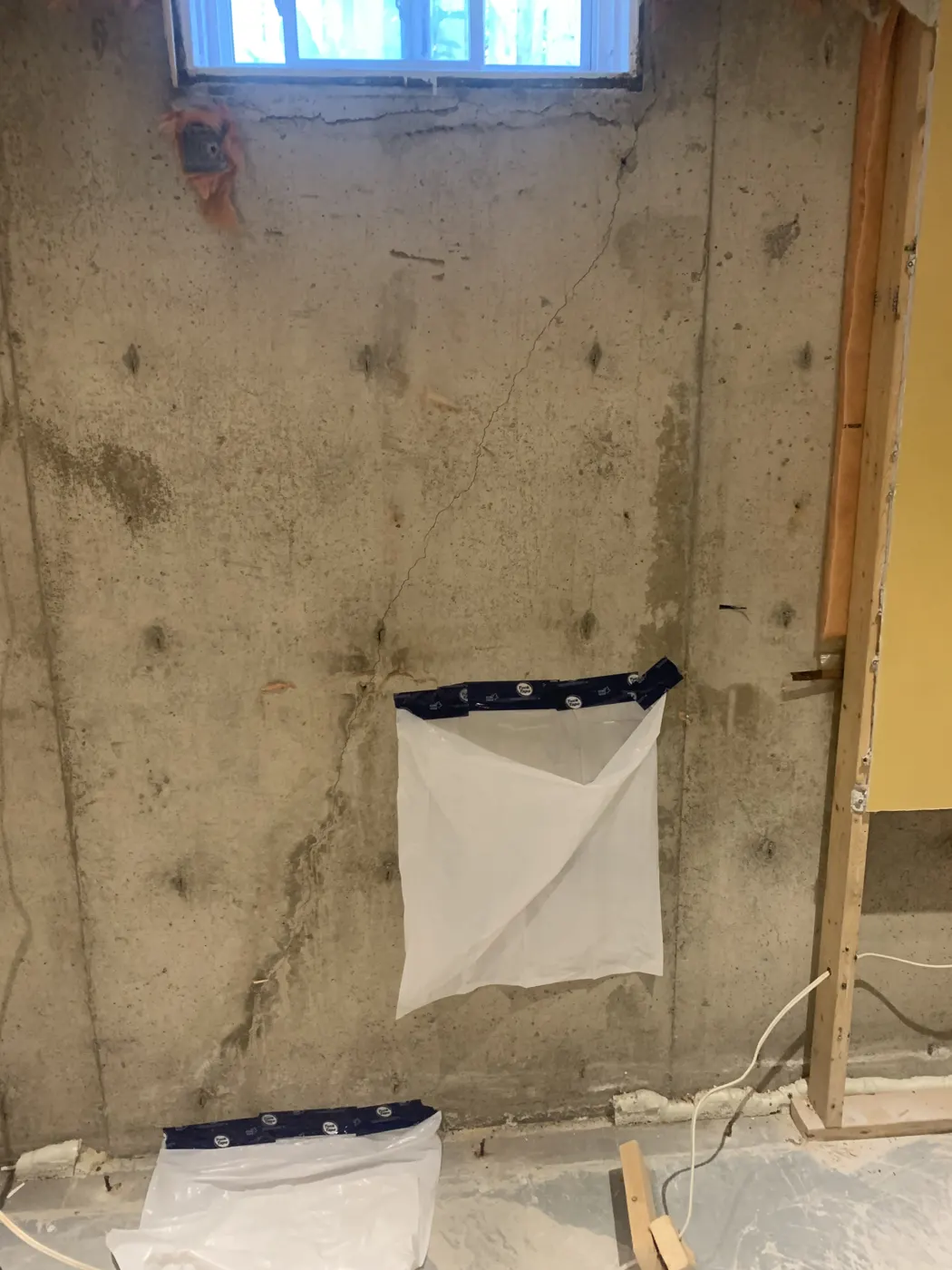 Diagonal foundation crack running from a basement window corner with moisture staining, before injection